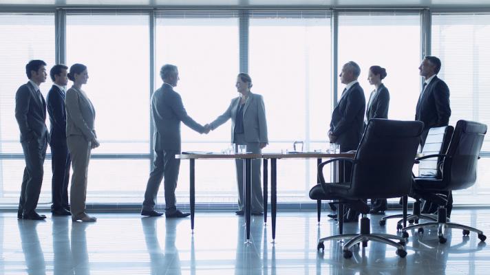 Two people shaking hands with six others watch