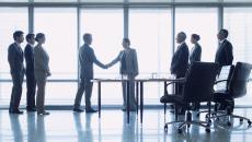 Two people shaking hands with six others watch