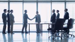 Two people shaking hands with six others watch