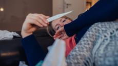 Person lying on their couch looking at a thermometer