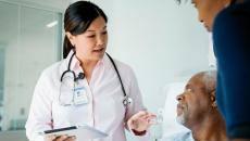 Doctor holding a tablet and standing by a patient and another individual 