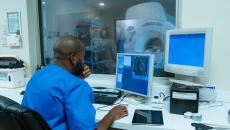 Healthcare provider sitting a room with a computer while there is a window for them to see a diagnostic imaging tool