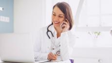 A doctor on the phone with a patient while checking their medical record on a laptop computer