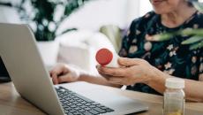 A close up of a person holding a pill bottle while using a laptop